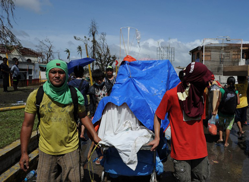 [Caption] Residents push an improvised trolley loaded with an injured relative as they head for a medical station in Tacloban City, Leyte province,central Philippines on November 10, 2013, three days after devastating Typhoon Haiyan hit the city on November 8.